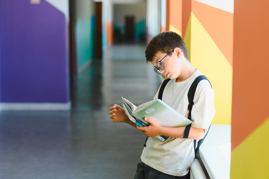 Schoolboy reading a book in the school corridor - Powered by Adobe