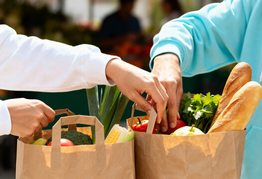 Close-up of people sharing fresh groceries at a farmers' market. Hands putting vegetables and fruit into paper bags. Healthy eating and food donation concept