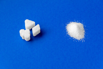 Sugar cubes and white granulated sugar comparison on blue background. Top view closeup.