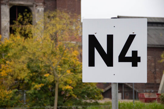 Large white sign displaying the letter N and number 4, set against a backdrop of autumn foliage and industrial architecture, indicating a location or direction