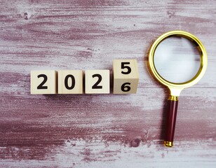 Wooden blocks showing 2025/2026 with a magnifying glass on a wooden surface.