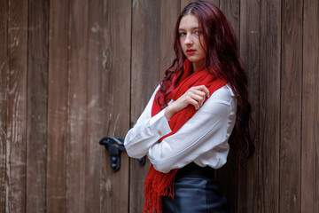 Fototapeta premium Young woman posing in front of wooden door with red scarf