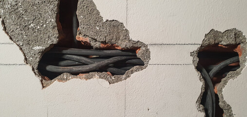 Two rough openings in a white wall showing thick, black electrical cables routed through the internal structure during residential electrical renovation or installation