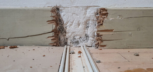 Low-angle close-up of a wall and floor during demolition, showing a trench with white powder, exposed wood splinters, and cable raceways on the floor