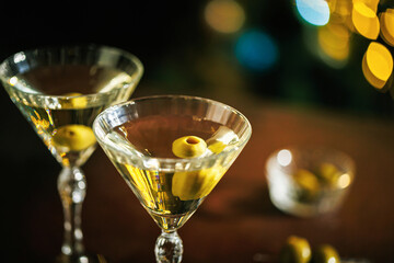 A close-up of a martini glass with a crisp cocktail and a floating olive, standing against a background of glowing golden lights, creating a warm and elegant mood.