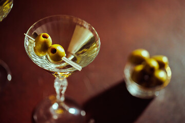 A sophisticated martini glass with green olives, illuminated by soft golden bokeh lights in a stylish setting.