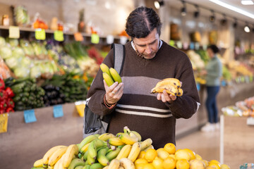 Male shopper carefully selects fresh bananas in a grocery supermarket