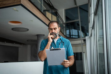 Doctor man with clipboard thinking serious in hospital