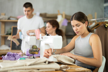 Attentive young female student of dressmaking courses working with sewing machine in workshop
