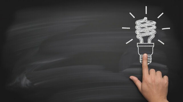 Innovative energy saving concept on a chalkboard with a finger pointing to a bright idea, sparking creativity and imagination for success in business
