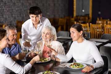 Elderly couple and young couple and adult woman have dinner and drink wine together in restaurant