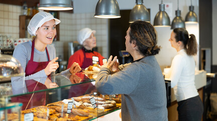 Bakery shop girl assistant talks to customer, answers clients questions and recommends fresh...