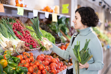 Portrait of female shopper choosing leek at supermarket counter