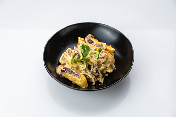 Potato wedges in creamy mushroom sauce with red onion, black bowl, studio top view