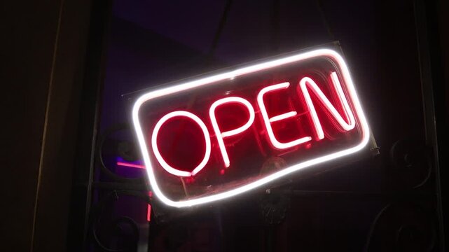A neon open sign hangs from the side of a window, perfect for use in commercial or hospitality settings