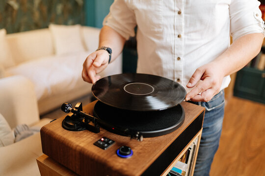 Man placing vinyl record on wooden turntable at home, cozy listening setup