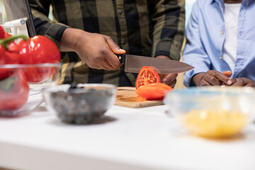 Close up of african american dad cutting tomatoes for his kids to cook together, slicing vegetables to sprinkle and ornate the homemade pizza. Home cooking and bonding as a family.