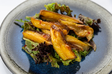 Roasted eggplant salad with sweet chili glaze on mixed greens, overhead on ceramic plate