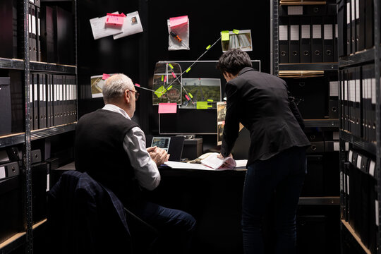 Team of criminologists interpreting fingerprints and classified evidence, organizing case files and witness statements while pursuing the authenticity of documents in a crime investigation.