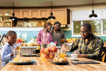 Black sweet family sharing croissants and orange juice in the morning, serving a rich colorful breakfast together under morning light. Young parents preparing the meal for their kids.