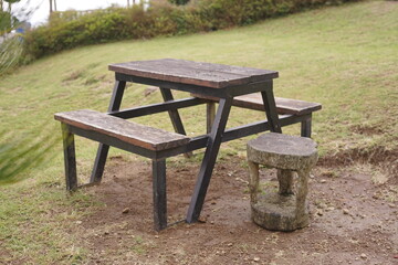 Rustic wooden picnic table with attached benches and a small natural stone stool nestled on a grassy slope, offering a serene spot for outdoor relaxation and simple gatherings in nature
