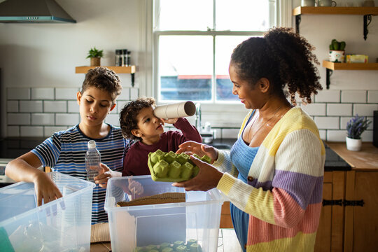 Adult mother with playful young sons recycling in home kitchen