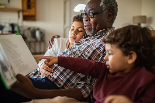 Senior grandfather reading to young grandsons at home, cozy and engaged - Powered by Adobe