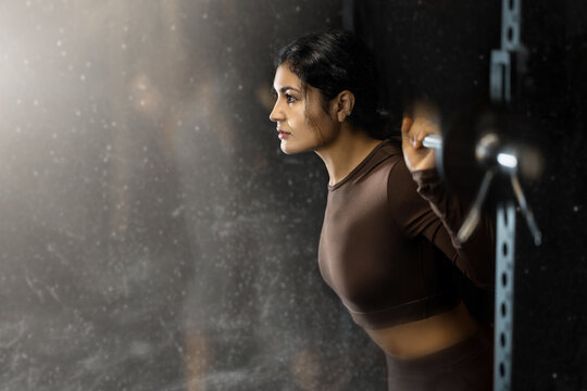 Determined Latina girl working out with barbell in well-equipped gym during training session