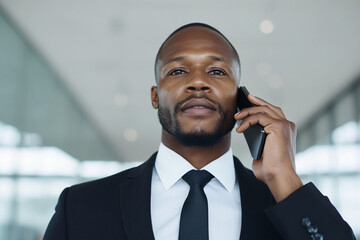 Professional Black businessman talking on a smartphone in a modern office. Confident corporate executive making a business call
