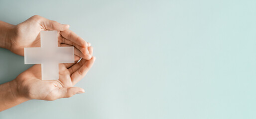Hands holding Plus cross model on blue background, medical healthcare, wellness support, positivity...