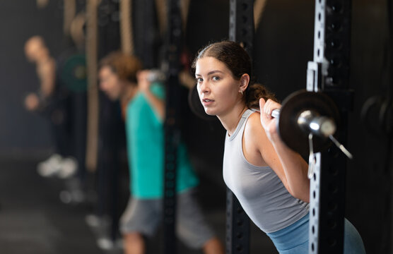 Motivated woman performs squats and lunges with a barbell on her shoulders in a power rack. Woman doing exercises for leg endurance in Crossfit classes