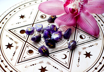 Scandinavian runes made of natural amethyst on a wooden altar for divination and an orchid flower. Fortune-telling, witchcraft, and spiritual esoteric practice.