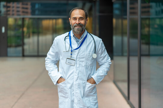Mature male doctor smiling confidently at hospital entrance