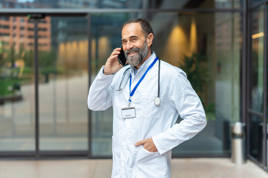 Smiling senior doctor using mobile phone outside hospital