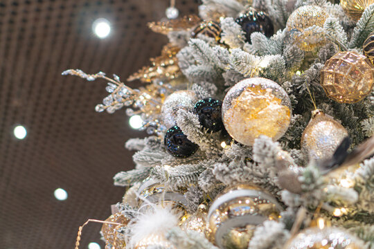 Centrally positioned, tall Christmas tree adorned with colored ornaments gold, blue, black, yellow and decorated for both New Years and Christmas Illuminated from above by multiple lights creatin