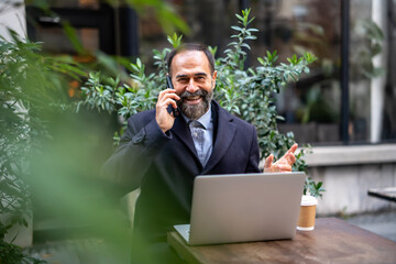Smiling mature man talking on phone using laptop