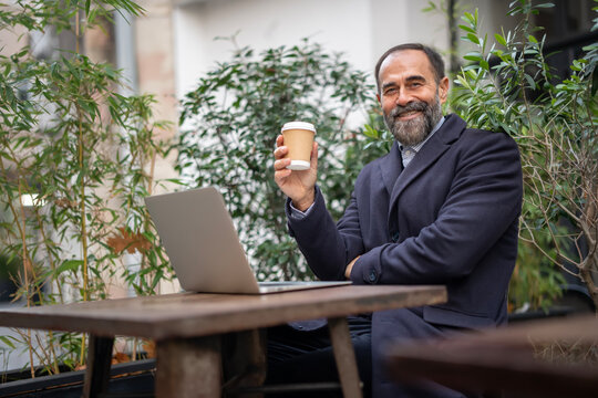Mature man working remotely, enjoying coffee at an outdoor cafe