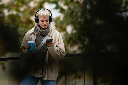 Woman enjoying music and coffee while using phone outdoors