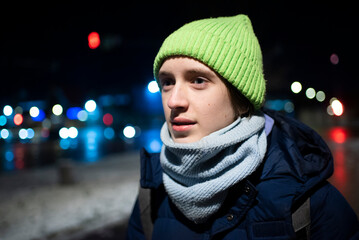 Portrait of a teenage boy in a green hat on an evening city street in winter.