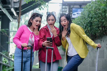 Astonished young women gazing at smartphone, their luggage besid