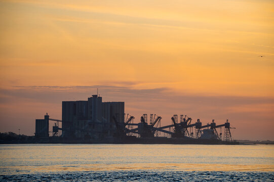 Large cereal grain silo port at Trafaria silhouetted against the setting sun as view from Belem, Lisbon.