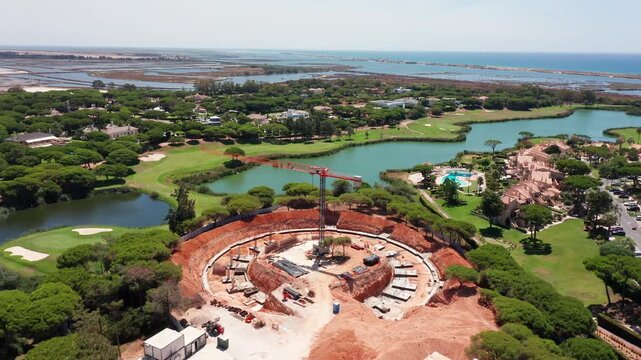 Aerial view of round construction site in Vale do Lobo, Portugal, surrounded by golf course, villas, lagoon and ocean. Concept of luxury coastal development and premium real estate infrastructure
