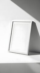 Minimalist white picture frame leaning against a wall with a shadow cast on a clean, bright surface creating a modern and sleek aesthetic