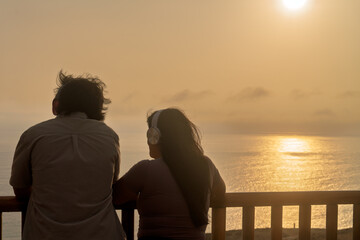 Couple watching sunset over ocean enjoying music