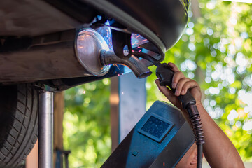 Mechanic welding new exhaust pipe on lifted car