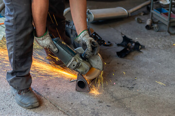 Worker using angle grinder cutting metal pipe in workshop