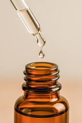 Vertical macro shot of a glass dropper releasing a clear liquid into an amber essential oil bottle, highlighting purity, precision, and natural skincare formulations ideal for beauty branding