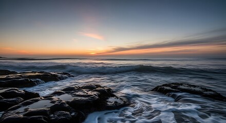 Serene ocean view during sunset with waves crashing against rocky shoreline and colorful sky in the background