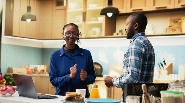Smiling black man and woman sharing a romantic dance in the kitchen, waltzing together on a passionate love song and flirting with each other. Holding hands and slow dancing, swaying. Camera B.