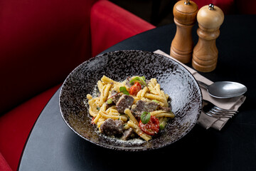 A delicious plate of pasta combines tender meat, ripe tomatoes, and fragrant herbs, beautifully arranged in a chic restaurant. The cozy ambiance invites enjoyment